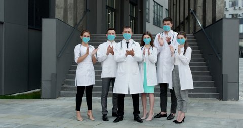 Medical staff from the hospital who are fighting coronavirus applaud back the people and police officers for their support. Group of doctors with face masks. Corona Virus and Healthcare Concept.