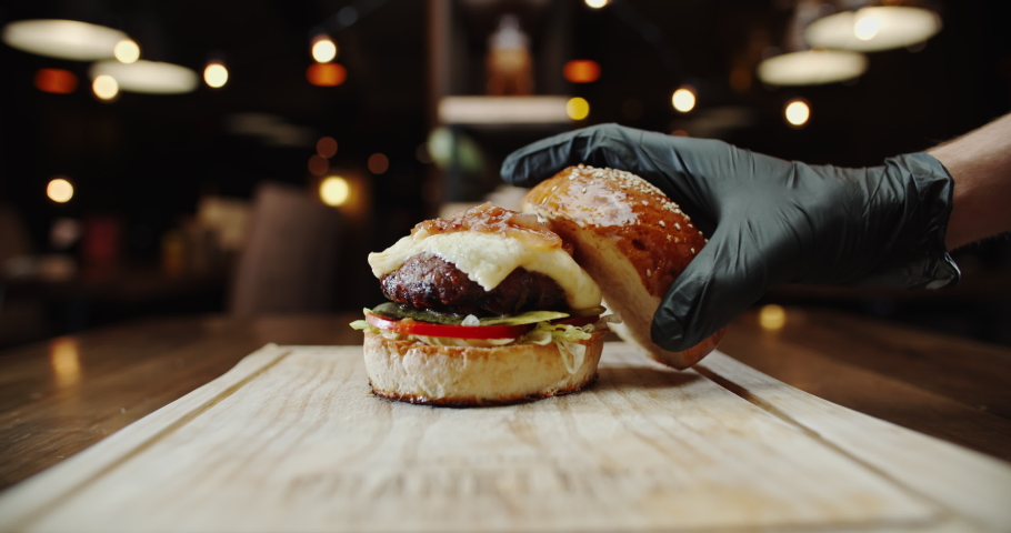 Close up shot of hand of chef putting a fresh top bun on large appetizing burger with various ingredients - food preparation, fast food concept 4k footage Royalty-Free Stock Footage #1057163434
