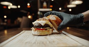 Close up shot of hand of chef putting a fresh top bun on large appetizing burger with various ingredients - food preparation, fast food concept 4k footage