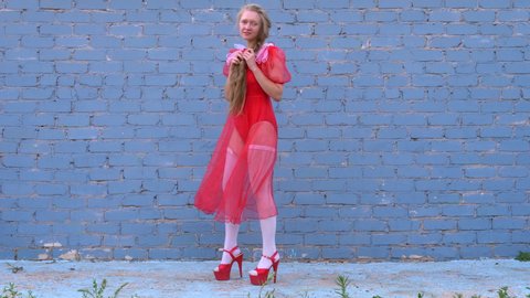 young woman in red shifon dress and swimsuit stands against gray wall in gust of wind