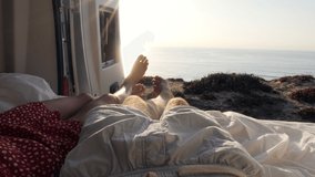 Point of view of couple's feet hanging out from van. Van lifestyle couple on camper van bed enjoys stunning ocean view  - Powered by Shutterstock - Get 15% off with code: PIKWIZARD15