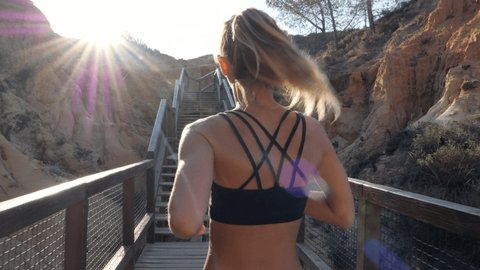 Attractive young woman athlete running in nature. Jogging exercising enjoying healthy fitness lifestyle, female runner at sunrise. Rea view running up a ramp of stairs 