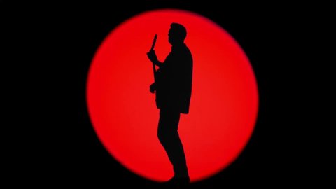 Shadow of an unrecognizable guitarist in a round beam of red light. Musician playing a rhythm guitar