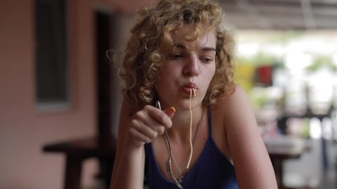 Curly Woman funny eating pasta and grimaces 