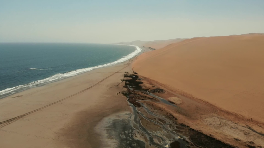 Aerial view of Sandwich Harbour in Namibia, where dunes meet the ocean, south of Walvis Bay,  during a sunny day in the Namib desert, famous travel destination Royalty-Free Stock Footage #1057185952