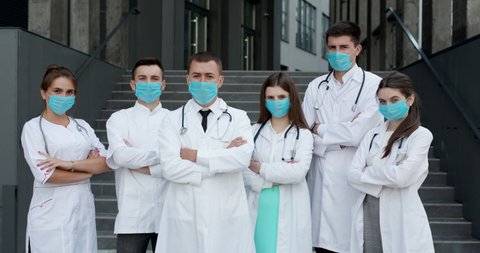 Group of doctors with face masks looking at camera, corona virus concept. Confident team of doctors in face masks standing with their arms folded and looking at camera
