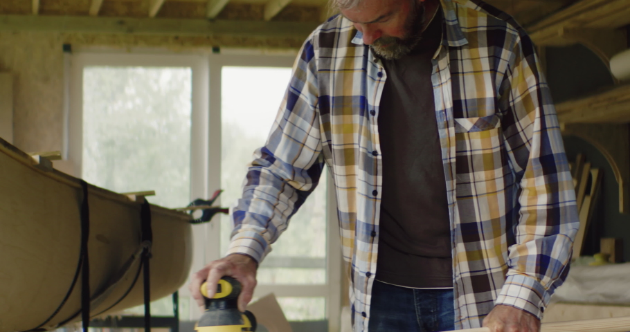 Mid 50s Caucasian male sanding a hand made canoe paddle in his workshop. Boat making hobby, small business owner