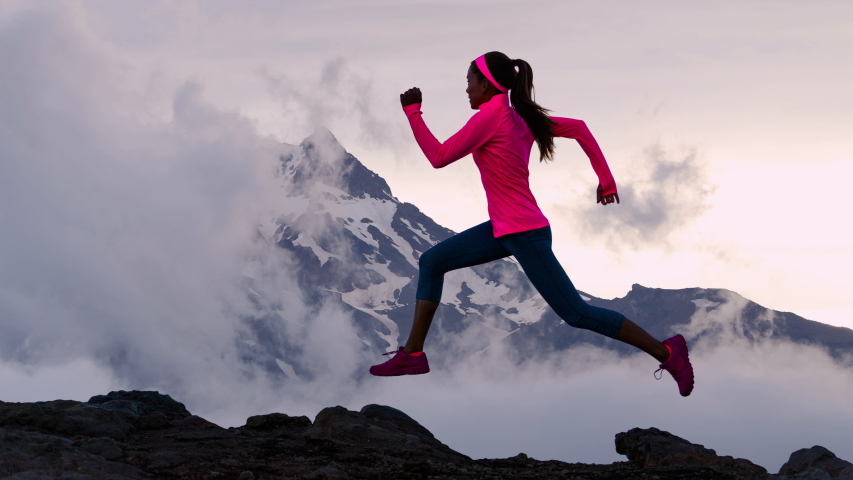 CINEMAGRAPH - seamless loop. Running woman runner athlete silhouette trail running with mountain summit background with clouds and peaks. Training outdoors active fit lifestyle. Looping Motion photo.