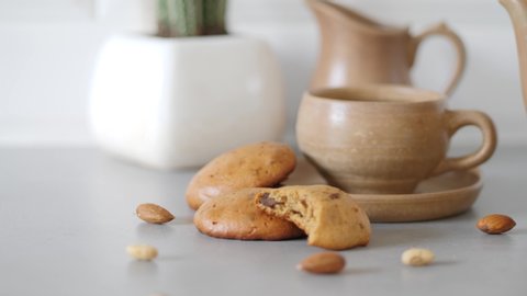 Three healthy cookies with a cup and a jug. Some almonds in the foreground and a cactus in the background.