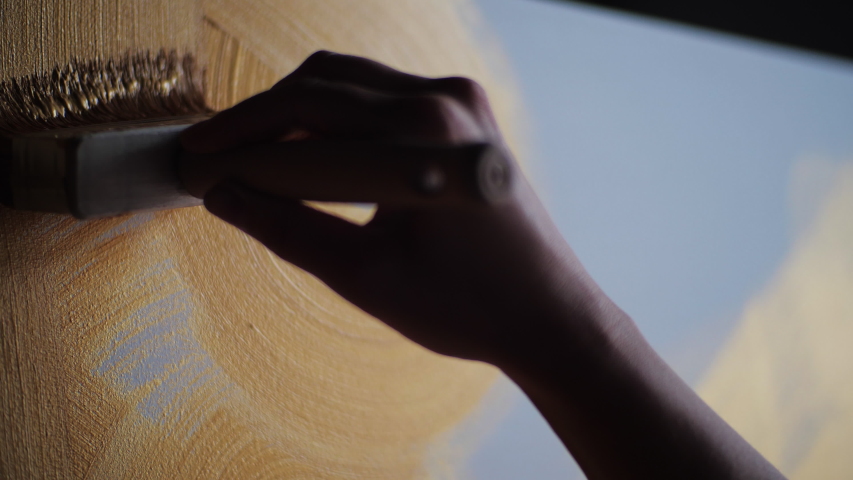 Woman hand artist paints draws, creating new art work on golden canvas enjoying process of painting. Wide brush applying yellow gold oil paint. Close up color palette materials choice for creativity Royalty-Free Stock Footage #1057193608