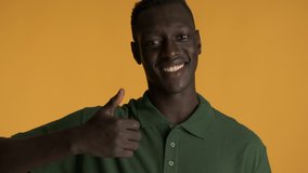 Handsome smiling African American guy joyfully showing thumbs up gesture on camera over colorful background. Like expression