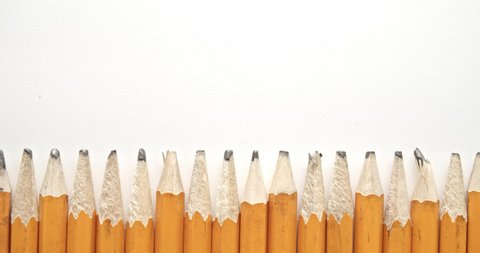 Panning across row of used and worn out yellow pencils with broken pencil tips, with one single and unique sharpened pencil.
