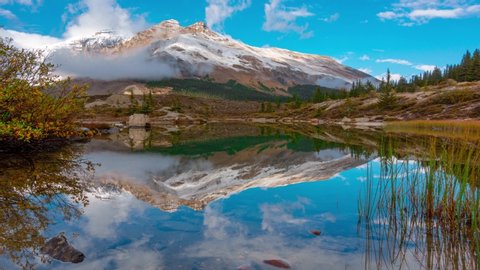 Lake Reflection of Massive Mountain Snow Covered Peak In Banff Mt K2 Time Lapse Brilliant blue sky reflected in a still glass mirror lake 4k