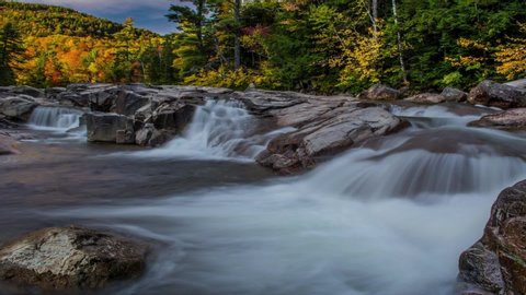 Smooth streaming river with bursting color of autumn leaves in orange, yellow and red small waterfall Time Lapse Full HD, Strong rushing river of rocks off of the Kancamagus highway in New England 