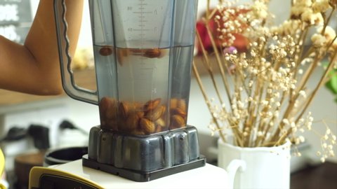 Woman mix grind almonds with water in blender  