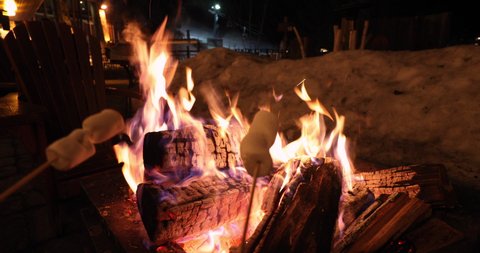 People roasting marshmallows in firepit having afterski fun leisure activity at Winter holiday ski resort. POV video of Couple grilling marshmallow stick in fire.