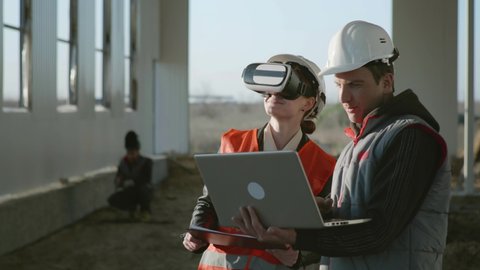 advanced technologies, specialists engineers and an architect in protective helmets woman in VR gadget explores the vertical reality of a new hangar project using a modern presentation on a