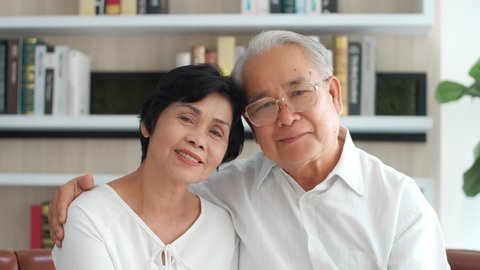 Asian elderly couple. Joyful nice elderly couple smiling looking at camera while being in a great mood, smiling healthy senior retired grandparents husband and wife happy faces embracing at home,