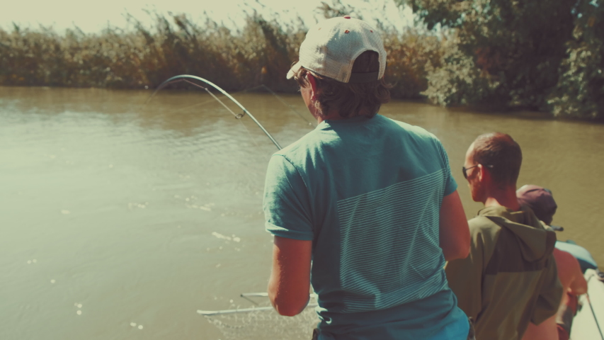 Tree amateur anglers fishing for carp on the river. Man caught the carp and fights with it