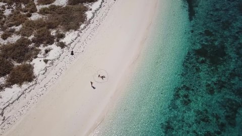 A drone shot of a couple lying on a pink sand beach in a heart drawn on the sand a small island near Maumere, Indonesia. Happy and careless moments. Waves gently washing the shore. Romance and love