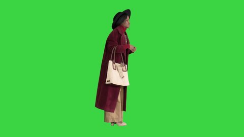 African american fashion girl in coat and black hat posing with a handbag on a Green Screen, Chroma Key.