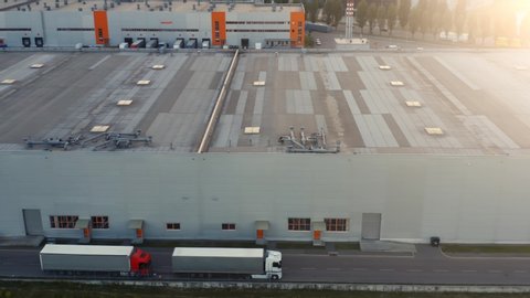 Big logistics park, loading hub. Semi trucks with cargo trailers standing along the warehouse and waiting for loading/unloading goods. Aerial side view 