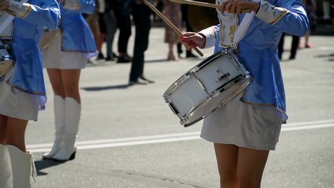 Street performance of festive march of drummers girls in blue costumes on city street. Close-up of female hands drummers are knocking in the drum of their sticks. Majorettes and marching band