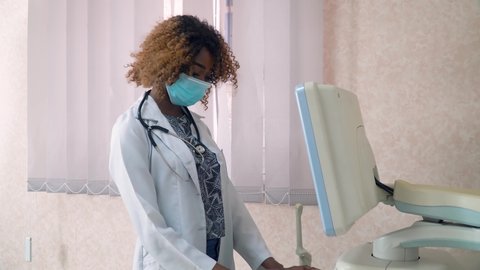 African american woman doctor in protective mask examines patient. Breast cancer diagnosis. Ultrasound devices monitor close-up. Possession of medical equipment