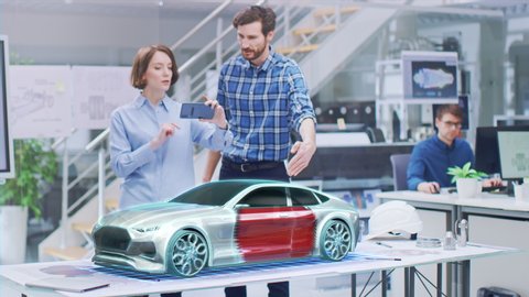 Industrial Design: Automotive Engineer and Designer Working on 3D Electric Car Design, Using Smartphone with Augmented Reality. Graphical Engine, Battery, Chassis, Body Collect into Full Vehicle