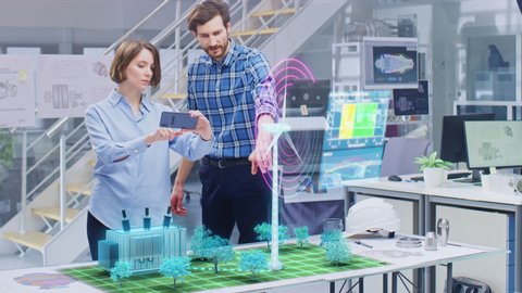 Green Energy Concept: Two Ecological Engineers Use Augmented Reality Smartphone to Design 3D Wind Turbine Park Hologram on the Table. Generating Sustainable and Renewable Clean Power for People