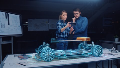 Two Automotive Engineers Use Augmented Reality Smartphone for 3D Electric Car Design. High Tech Green Energy Automotive Vehicle Construction. Concept VR AR Graphics