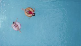 Distant shot of two beauty brunette in red swimwear relaxing at home or hotel pool, swimming, making waves and sitting in rubber inflatable circles, moving arms, tanning, enjoying vacation, top view - Powered by Shutterstock - Get 15% off with code: PIKWIZARD15