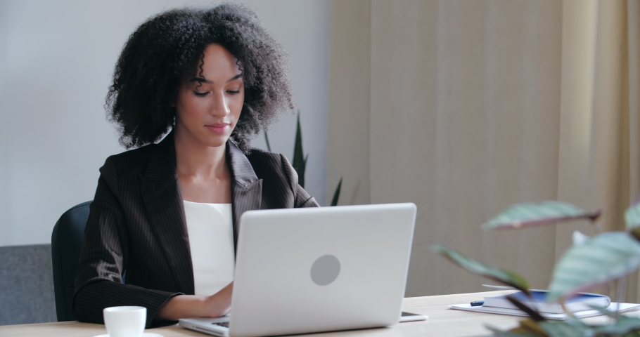 Serious African American student freelancer wear black jacket sitting at desk at home, typing on laptop keyboard, surfing Internet network, successful working online, booking tickets, close up Royalty-Free Stock Footage #1057233562