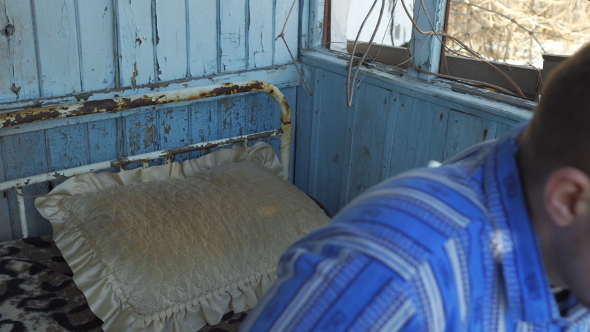 Young man in pajamas lying on an old bed in a dirty, dilapidated house
