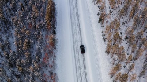 Bird’s eye view of car driving on countryside off road on winter vacation getaway, top view of 4x4 suv vehicle on white frozen wanderlust destination on journey. North nature landscape in winter