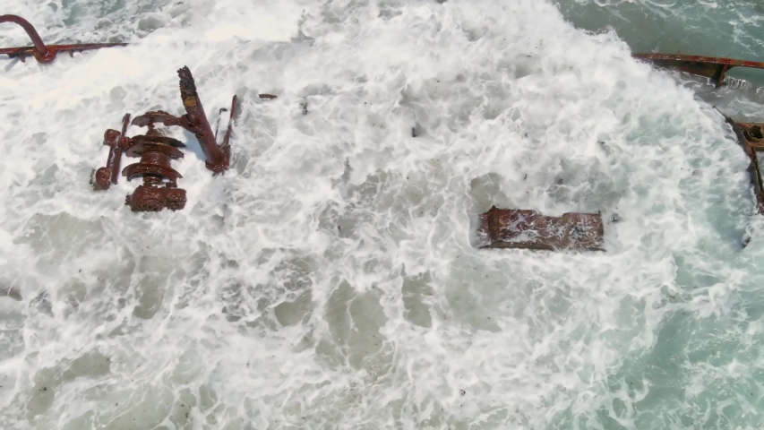Waves crashing on a rusty shipwreck on Ha Bonim beach in Israel, aerial drone view, slow motion