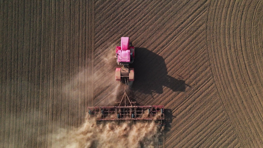 Shooting from drone flying over tractor with harrow system plowing ground on cultivated farm field, pillar of dust trails behind, preparing soil for planting new crop, agriculture concept, top view Royalty-Free Stock Footage #1057237972