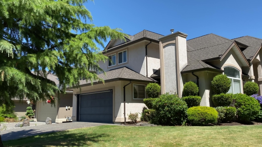 Establishing shot of two story stucco luxury house with two garage doors, big tree and nice landscape in Vancouver, Canada, North America. Blue sky. Day time on September 2020. Pan left. H.264. | Shutterstock HD Video #1057241575
