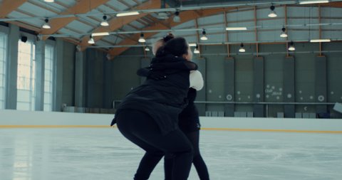 Young small girl professional figure skater parcticing jumps with her trainer on ice. Shot on RED cinema camera with 2x Anamorphic lens, 75 FPS Slow motion