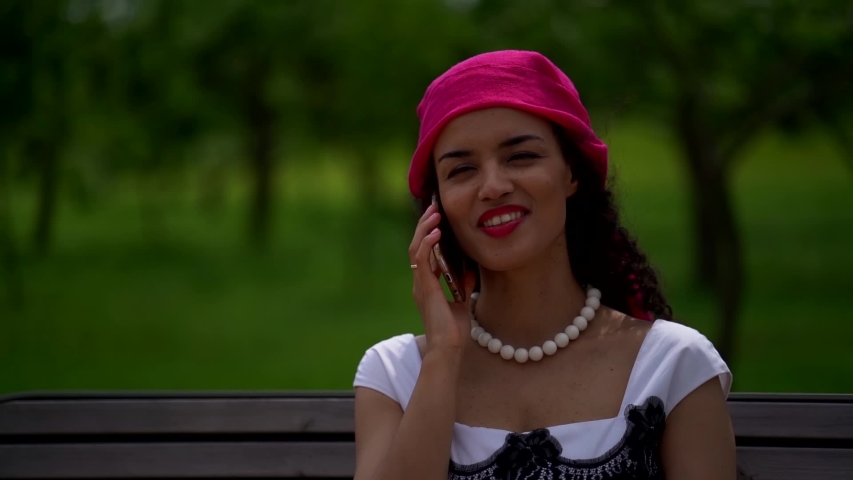 Portrait of an African woman who is on the street and sitting on a bench, talking on the phone and smiling