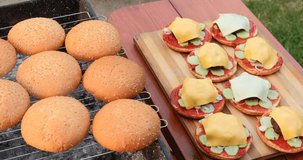 Hamburger holiday menu. Burgers are prepared in outdoors from buns, fried cutlets, vegetables, slice of cheese, tomato, ketchup, sauce. Chef man preparing the fresh burger. 4K UHD video