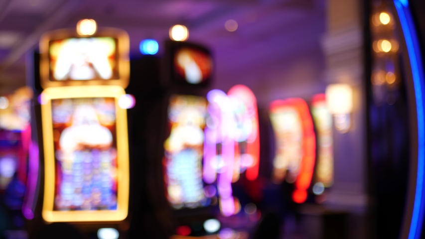 Defocused slot machines glow in casino on fabulous Las Vegas Strip, USA. Blurred gambling jackpot slots in hotel near Fremont street. Illuminated neon fruit machine for risk money playing and betting. Royalty-Free Stock Footage #1057248316