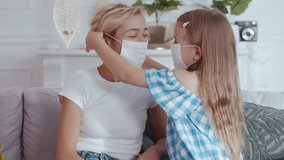 Cute caring young little girl wearing respiratory mask for her mother's face. Happy woman young beautiful mom with daughter protected from coronavirus. - Powered by Shutterstock - Get 15% off with code: PIKWIZARD15