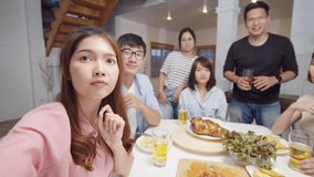 Group of young Asian people look at camera, remote video call greeting with friend at home dinner party. Point of view vlog or selfie camera. New normal lifestyle, social distancing concept
