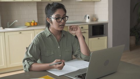 Indian woman online tutor remote teacher wearing glasses speaking to webcam chat explaining remote course video call school lesson looking at laptop virtual conference meeting work at home office.