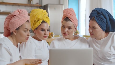 Four beautiful overweight girls with towels on their heads shopping online on laptop during pajama party
