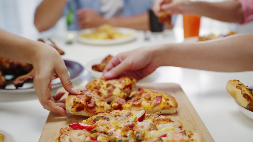 Close up shot of pizza on table, young friends group having lunch sitting around and picking up a portion at home. Asia family party eating food at dining table. Celebration holiday and togetherness. | Shutterstock HD Video #1057257709