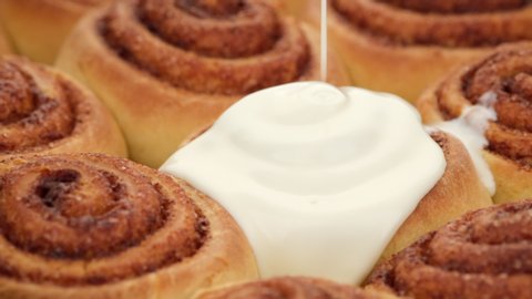 pouring fluffy frosting on Freshly baked cinnamon rolls or Cinnabon close up. Sweet cream cheese frosting pouring on cinnamon rolls