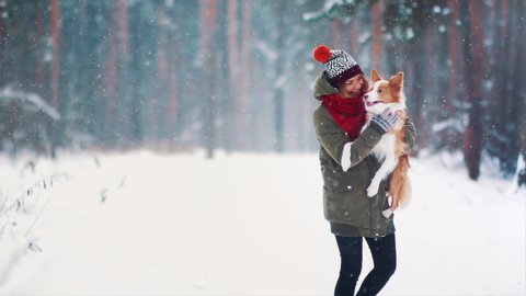 Animal love. Happy young woman playing with her border collie dog in snowy winter forest. Friendship of a female and a pet. Having fun together. Dogs are best friends. Cheerful puppy hugs her owner.