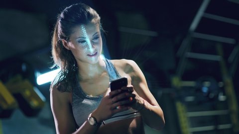 Young Woman In Sportswear Holding Smart Phone Texting Indoors Fitness Face Detection 3D Scanning Biometric Facial Recognition ID 5G Connections Future Shot Red Epic 8k
